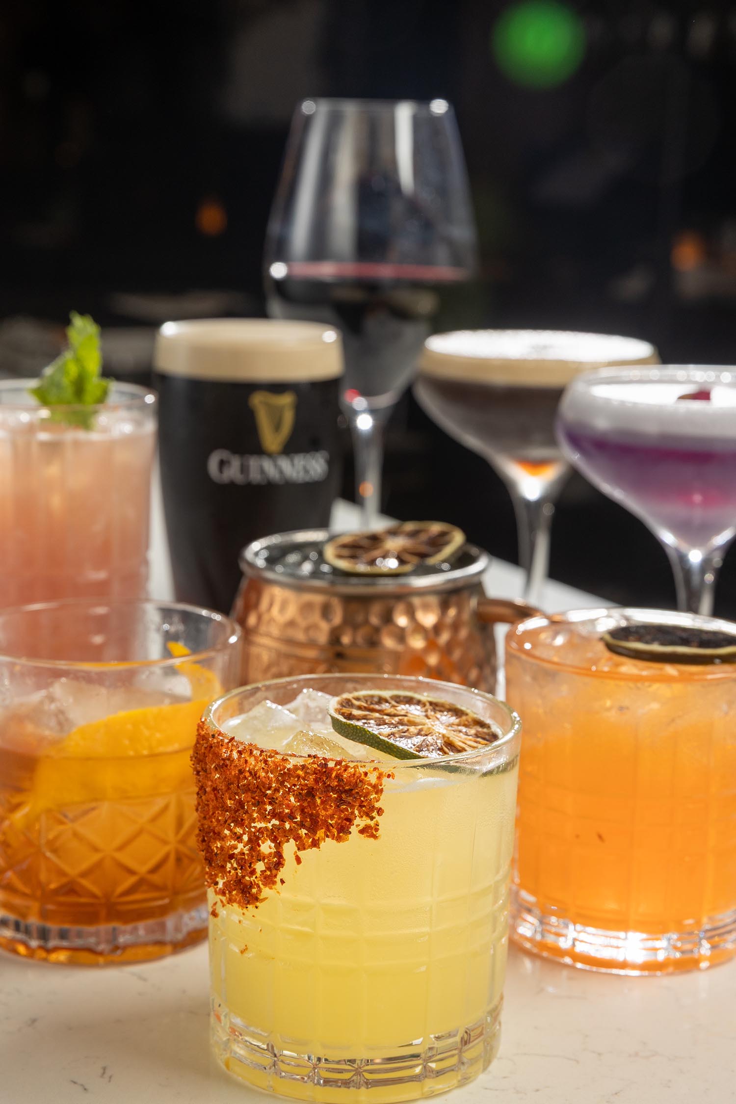 Variety of colorful cocktails and drinks including a Guinness beer and a glass of red wine on a table.